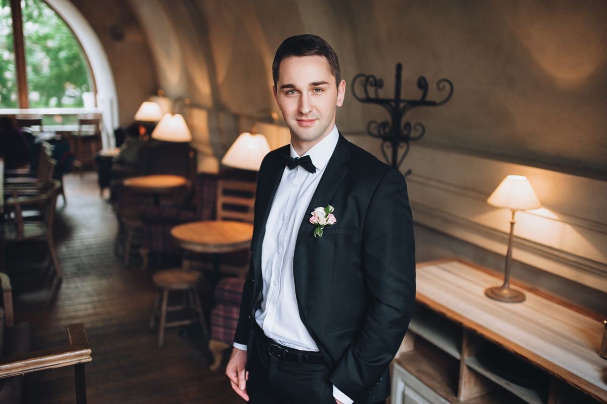 Beautiful and tall groom in the interior, in a black suit. The groom looks at the frame in the restaurant.